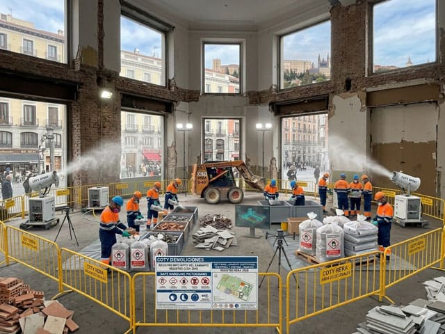 Equipo de Coty Demoliciones con EPIS naranjas realizando el vaciado técnico y desmantelamiento de un local de hostelería en una zona comercial de Madrid, con maquinaria eléctrica y control de polvo activo.